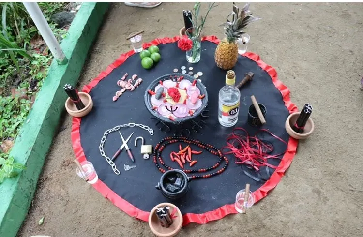 Oferenda sobre toalha preta com babado vermelho, com correntes, cadeado, tesoura, guia de contas, pimentas, abacaxi e velas