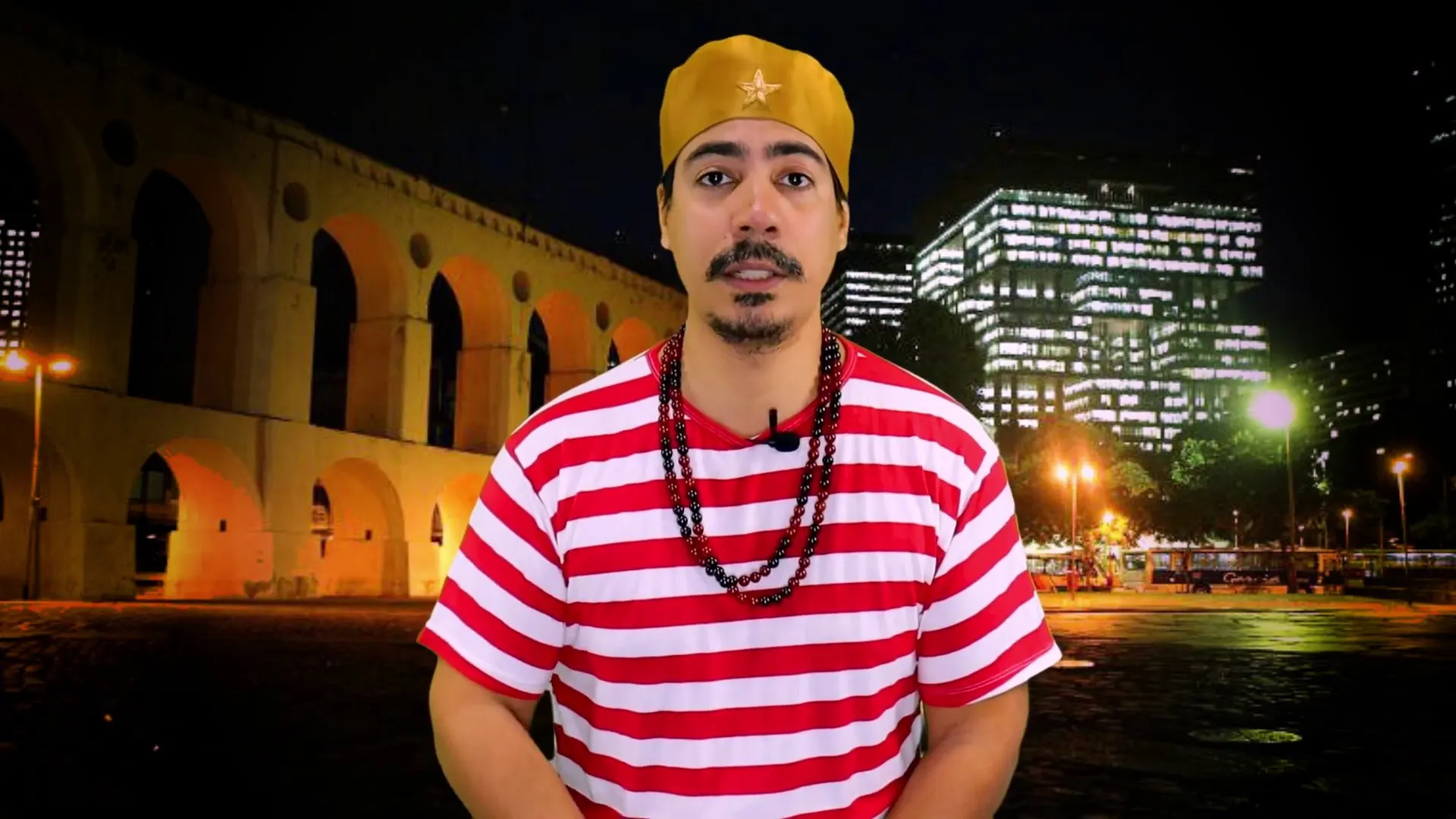 Bruno Amorim de camisa listrada vermelha e branca diante dos Arcos da Lapa, à noite