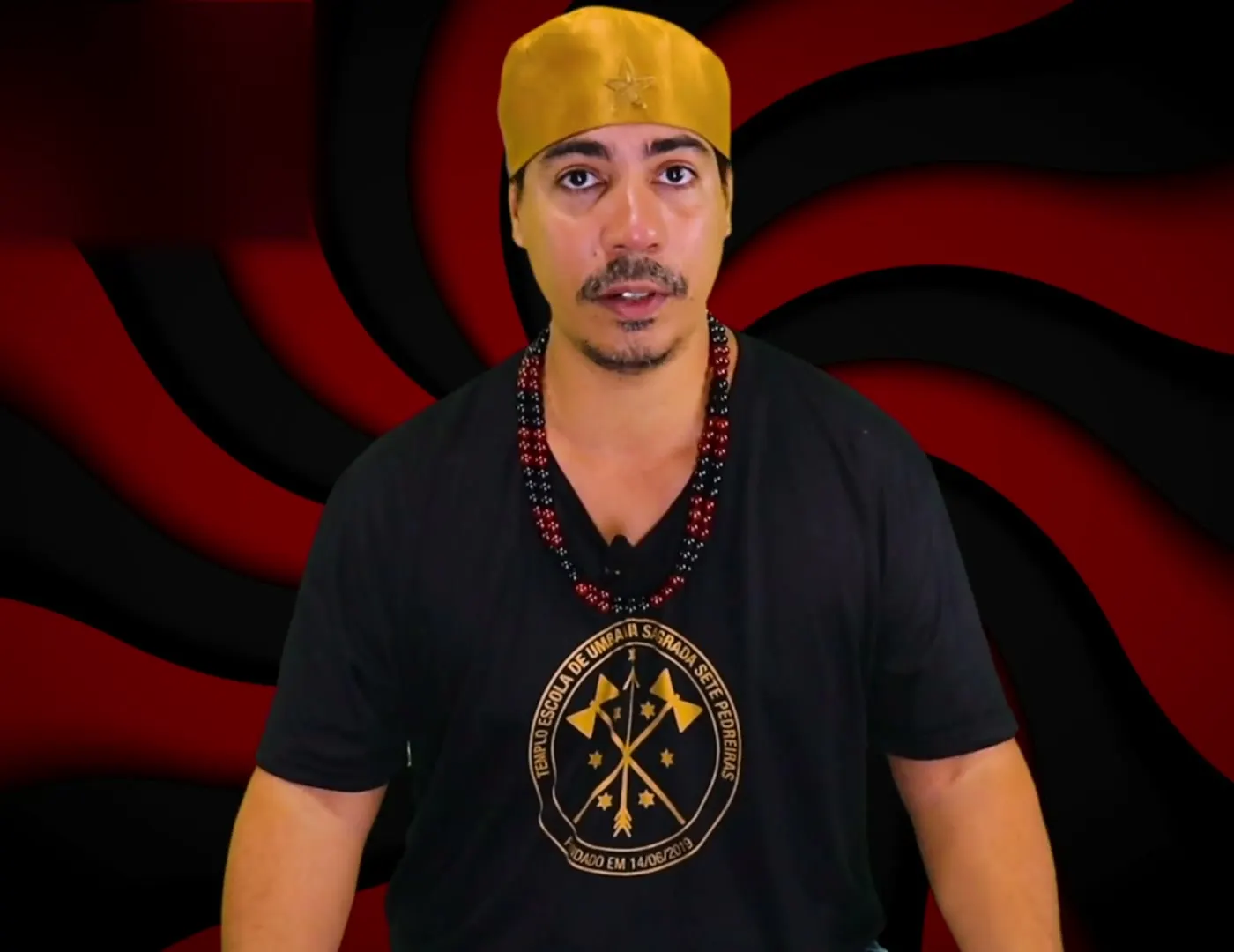 Bruno Amorim, de camiseta preta e guias vermelhas e pretas, diante de um fundo vermelho e preto