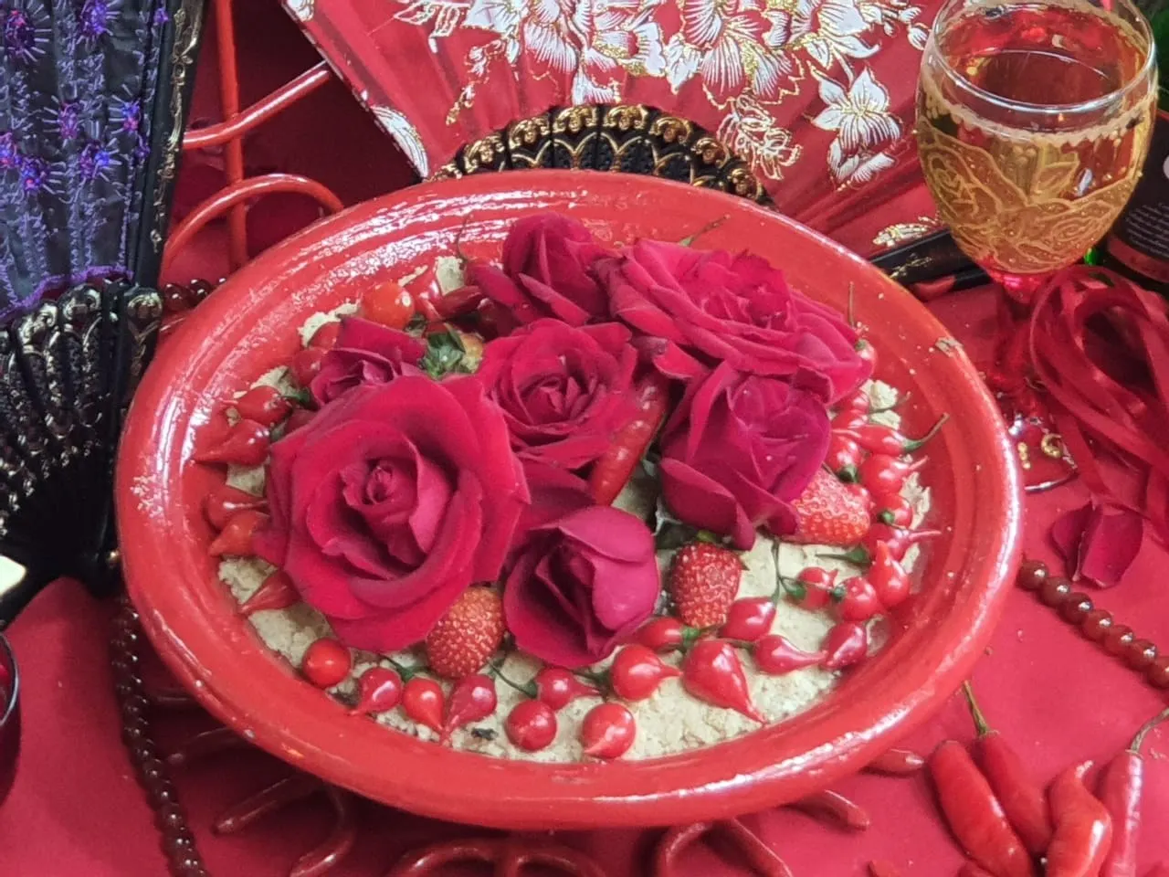 Alguidar vermelho com farofa, rosas vermelhas, morangos e pimentas, ao lado de um leque