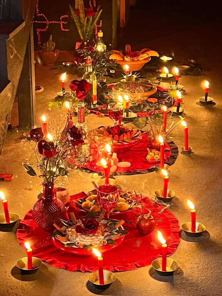 Várias oferendas sobre toalhas vermelhas, à noite, com rosas, frutas e dezenas de velas vermelhas acesas