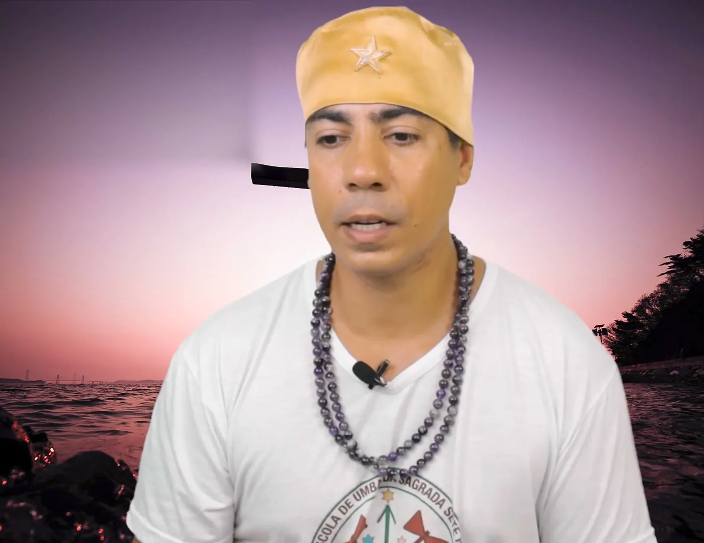 Bruno Amorim, de camiseta branca e guias escuras, diante do mar ao entardecer