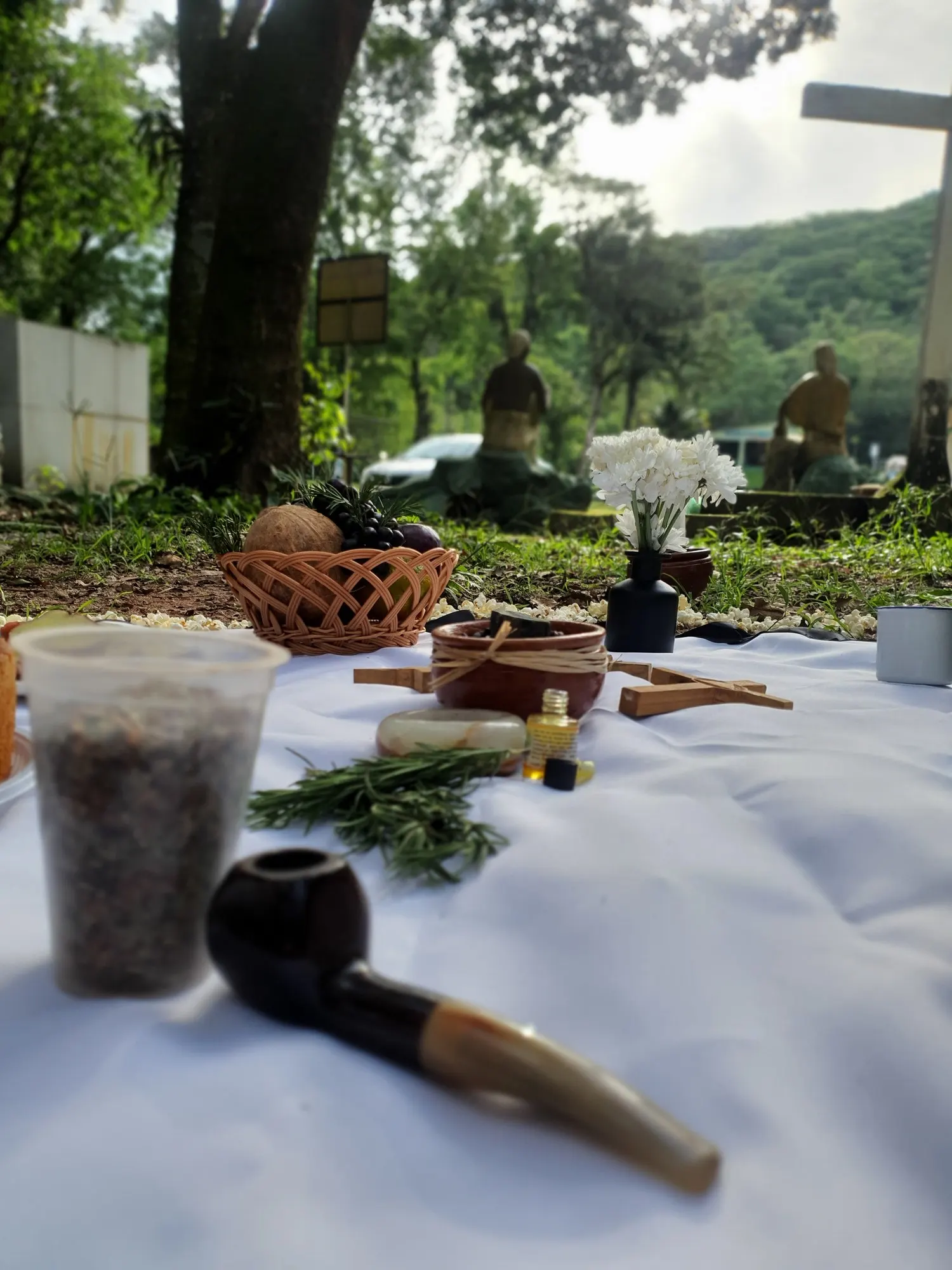 Cachimbo e raminhos de alecrim sobre toalha branca, com a oferenda ao fundo