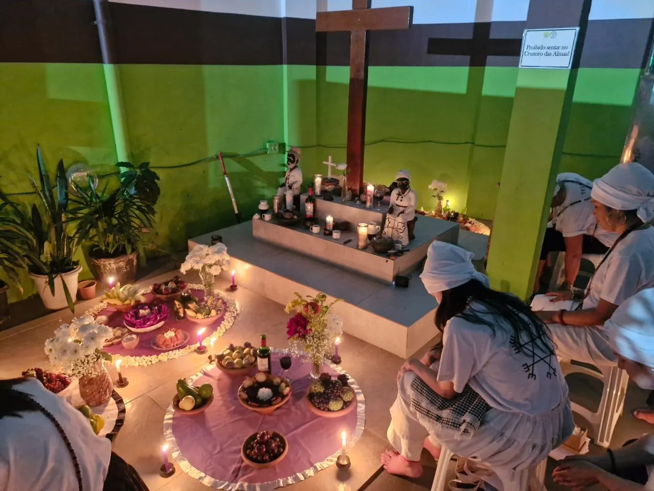Médiuns de branco diante do Cruzeiro das Almas do templo, com oferendas em toalhas lilás e velas acesas
