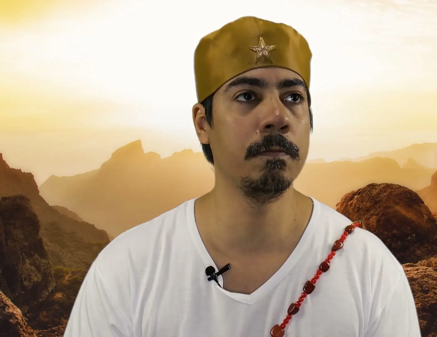 Bruno Amorim, de camiseta branca e gorro dourado, diante de montanhas ao sol