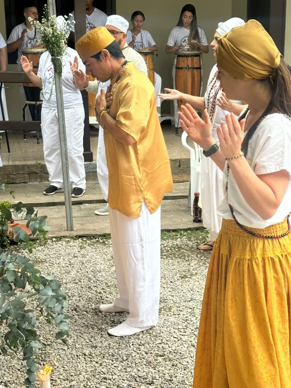 Abertura da gira de formatura da Turma 2: Bruno Amorim, de dourado, se curva com as mãos no peito; à direita, Flávia Amorim, de saia amarela, e ao fundo os atabaques da curimba