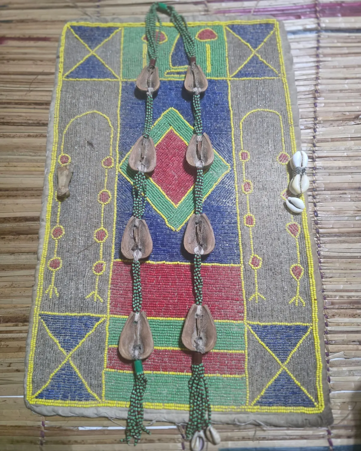 O Opele, corrente com oito sementes, estendido sobre um tapete bordado de contas coloridas, com búzios ao lado